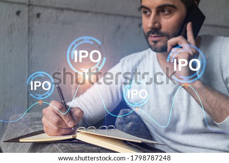 Handsome analyst in casual long sleeve talking phone, taking notes at office workplace try to analyze IPO project. Double exposure. Initial public offering hologram. Royalty-Free Stock Photo #1798787248