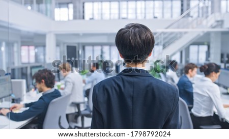 Back Shot of a Young Manager Walking Pass His Business Colleagues and Supervise Their Work. Diverse and Motivated Business People Work on Computers in Modern Open Office. Royalty-Free Stock Photo #1798792024
