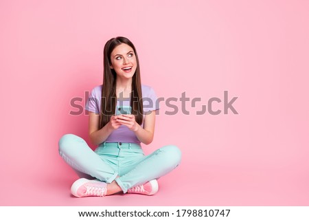 Full size photo of excited girl sit floor legs crossed use cellphone enjoy texting typing social network feedback wear turquoise violet purple trousers isolated pastel color background