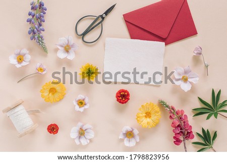 Blank paper card mock, flower buds, ribbon, envelope on beige background. Wedding invitation, holiday celebration concept.