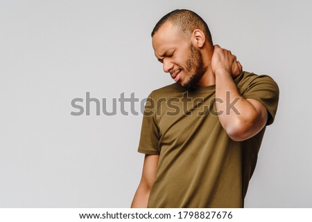 young african american man in green t-shirt on grey background feels physical discomfort for neck pain massaging tensed muscles Royalty-Free Stock Photo #1798827676