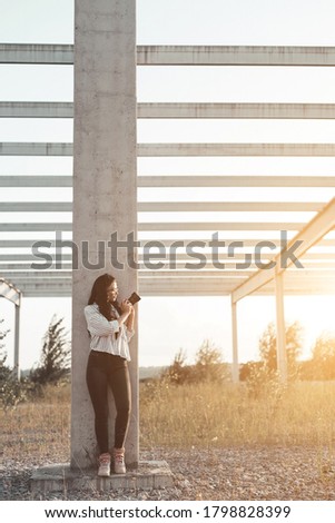 Young woman photographer leaning on concrete post taking a photo