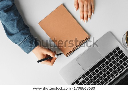 Female hand writing in a notebook on table with laptop, view from above