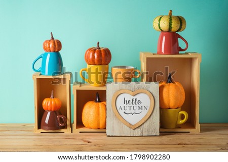 Hello Autumn concept with heart shape photo frame and pumpkin decor on wooden table over blue background.