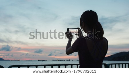 Woman use of mobile phone to take photo at sunset time