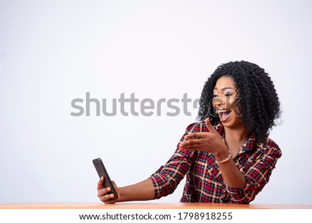 pretty young black woman sitting using her phone, looking surprised and excited