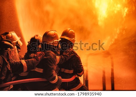 Firefighter using extinguisher or Twirl water fog type fire extinguisher to spray water from hose for fire fighting with fire flame on fuel and control fire for safety in plant of industrial area. Royalty-Free Stock Photo #1798935940