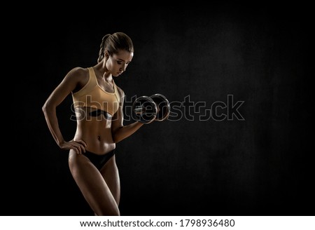 young fitness woman execute exercise with dumbbells on black background with empty space for text. Gym concept