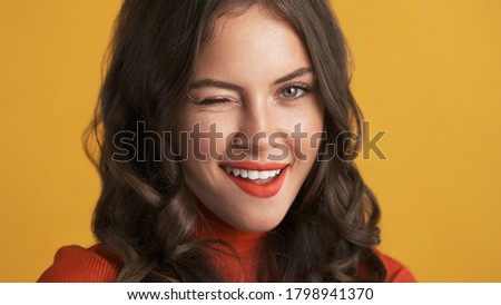Close up attractive flirty brunette girl with red lips winking on camera over colorful background  