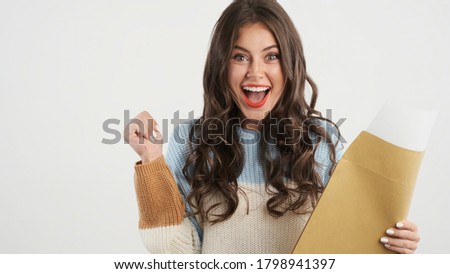 Pretty excited brunette girl in sweater opening envelope with exam results and happily rejoicing on camera isolated