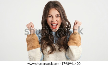 Beautiful excited brunette girl in cozy sweater emotionally rejoicing on camera over white background