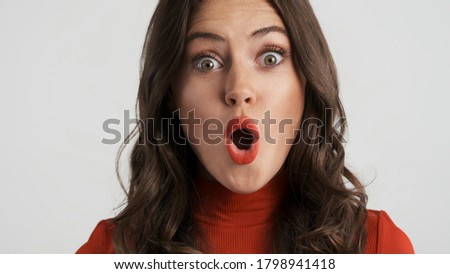 Portrait of beautiful excited brunette girl amazedly looking in camera over gray background. Wow expression
