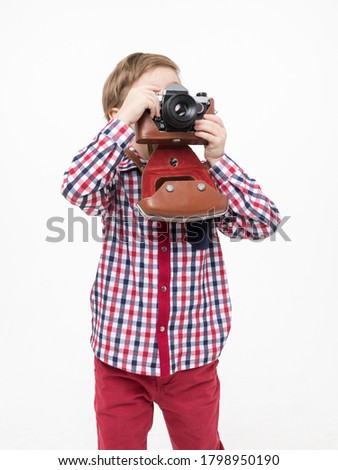 Adorable smart photographer kid holding black camera in hands looking through the lens on white background	
