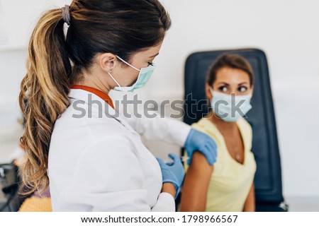 Female doctor or nurse giving shot or vaccine to a patient's shoulder. Vaccination and prevention against flu or virus pandemic.  Royalty-Free Stock Photo #1798966567