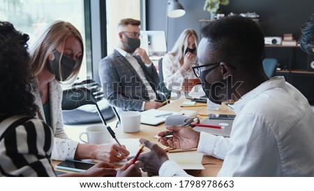 Office workplace with COVID-19 safety. Young multiethnic business people meeting at work wearing multi-use face masks. Royalty-Free Stock Photo #1798978663