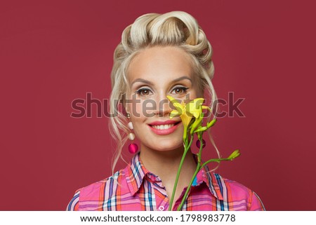 Pinup woman smiling and holding vivid yellow flower. Beautiful female model with pink lips make up and vintage fashion hairstyle on red background