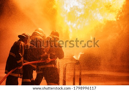 Firefighter using extinguisher or Twirl water fog type fire extinguisher to spray water from hose for fire fighting with fire flame on fuel and control fire for safety in plant of industrial area. Royalty-Free Stock Photo #1798996117