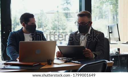 Business meeting during COVID-19 pandemic. Two young male Caucasian partners talk at modern office in face masks. Royalty-Free Stock Photo #1799001649