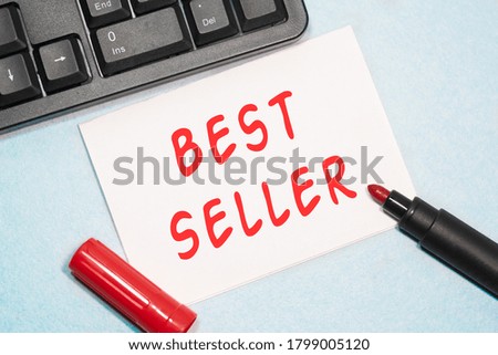 BEST SELLER text on the business card written in red marker near the keyboard on a blue background