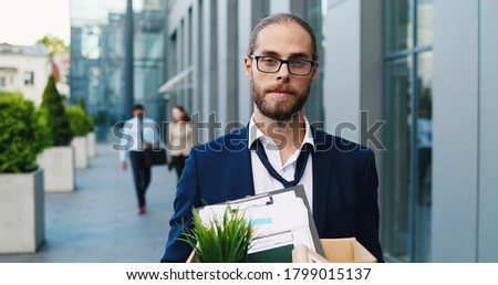 Portrait of sad Caucasian man in glasses, white-collar worker at street holding box with stuff. Fired male. Upset manager dismissed from work. Economic crisis of unemployment. Firing from job.