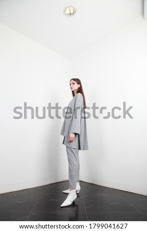 Catalog style studio shot of a Caucasian female fashion model wearing cotton grey summer autumn  suit. She is posing to show trendy style of the outfit or clothing. Side view, model