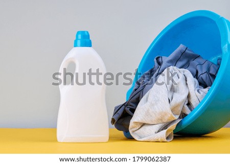 detergent bottle with stack of a colored clothes for laundry cleaning and washing service. background backdrop. copy space. studio shoot. laundry concept.