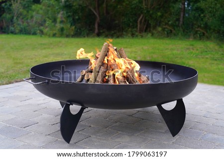 Iron fire pit and burning fire in  a garden . Royalty-Free Stock Photo #1799063197