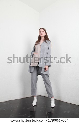 Full shot of a brown haired European lady with long hair in a summer cotton two piece suit, standing in a simple interior with white walls, studio photography, copy space for fashion industry campaign