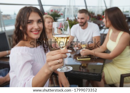 Selective focus on a wine glass in the hand of cheerful woman drinking with friends