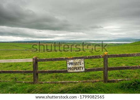 Old worn warning sign "Private property" on a fence by a green field, Grey cloudy sky, West of Ireland. Nobody.