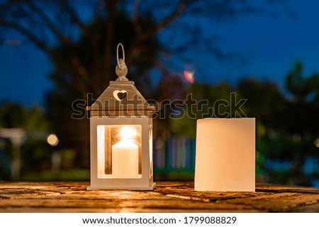 lamp with lit candle on old wood table. plain white sheet of paper. autumn background. night photography