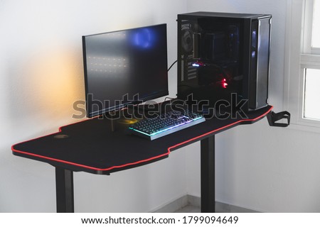 Gaming PC in a gaming desk. The pictures shows a complete computer for a gamer, with a fast response monitor, RGB lights, keyboard, mouse and a case.