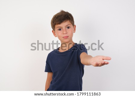 Beautiful kid boy wearing casual t-shirt standing over isolated white background smiling cheerful offering palm hand giving assistance and acceptance.