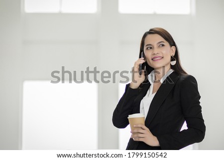 Portrait of a young Asian business woman talking over cellphone and holding cup of coffee in business building. Photo of beautiful girl in casual suite with phone and cup of coffee. Stock photo