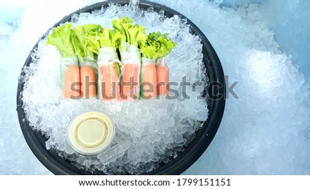 Salad rolls, photo of salad dressing, green vegetables followed by ice. There is a black circle of a saucer In the upper left corner of the picture there is a strong white light shining down. Against 