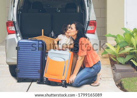 Little girl kissing her mother near their car while preparing to vacation. Shot in the garage house