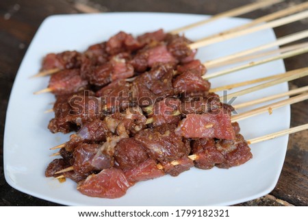 Sate Sapi beef satay on a white ceramic plate. The satay has not been roasted over coals. Traditional Indonesian food made from cut beef, seasoned with soy sauce, garlic, chilies, then skewered.