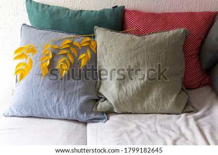 Сushions on the sofa with branch of yellow leaves as seasonal decoration. Autumn interior 
