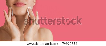 Close up photo of a caucasian woman using cotton discs on her face posing near pink studio wall with free space