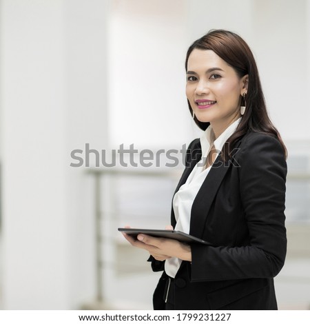 Portrait of a young cheerful businesswoman surfing social network on digital tablet in front of office during break. Asian business woman standing in office building. Stock photo