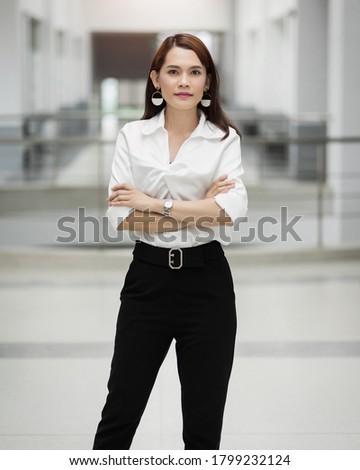 Portrait of a pretty middle age businesswoman standing Portrait of a cheerful middle-age businesswoman in business suit standing in the company building with confidence arms crossed. Stock photo