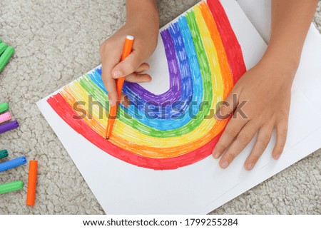 Little child drawing rainbow on floor indoors, closeup. Stay at home concept