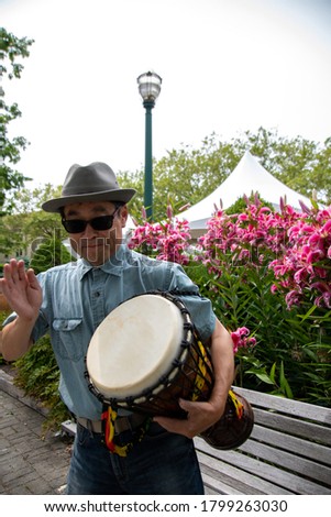 A picture of an Asian man in-the-middle of hitting a djembe.       