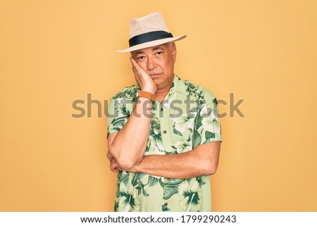 Middle age senior grey-haired man wearing summer hat and floral shirt on beach vacation thinking looking tired and bored with depression problems with crossed arms.