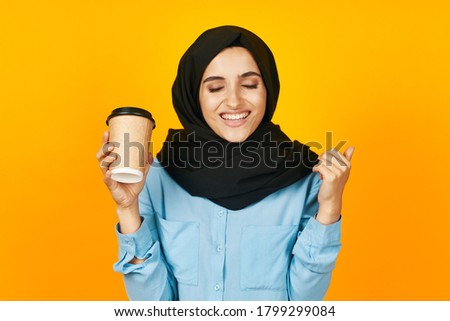 Cheerful Woman in black hijab cup with coffee yellow background