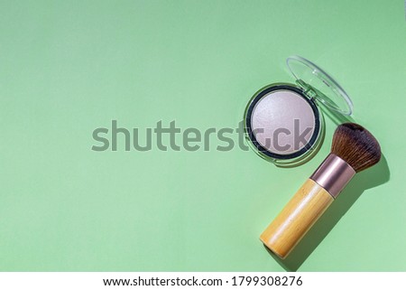 Makeup brush and powder on a green background. Cosmetics and fashion concept. Hard light. Flat lay, copy space