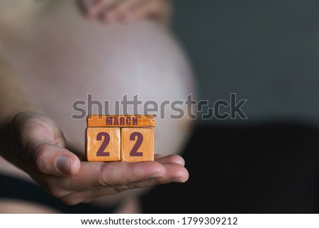 march 22nd. Day 22 of month, planned date of birth. Month and day placed on wood calendar in pregnant womans hand. spring month, day of the year concept.