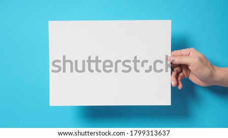 Empty space for text.Hand is holding blank A4 paper on blue background.