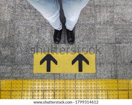 feet are standing on the yellow arrow sign of sky train platform in Bangkok. 