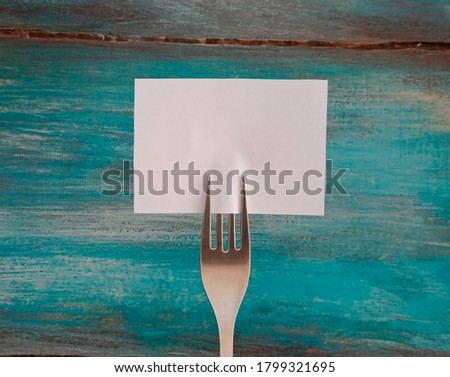 A fork with a blank card with space for text. Creative layout for business food concept. A colored wooden tray in the background.